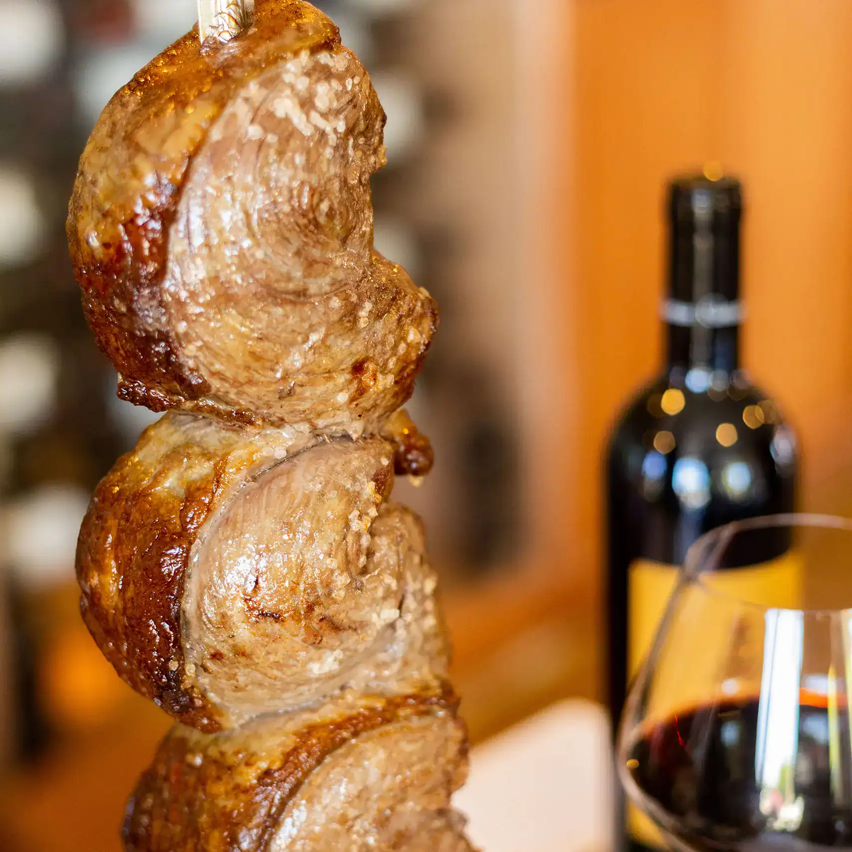 Picanha steak folded on a churrasco skewer with coarse salt crust, served with red wine at Adega Gaucha